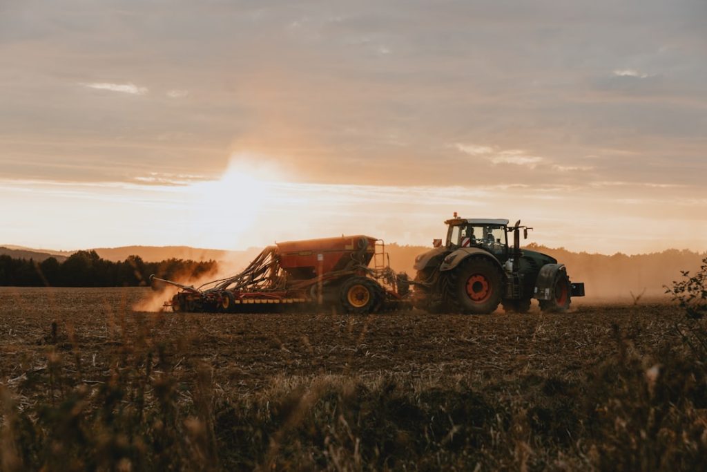 Tractor with attached seeding machine sowing seed on the plowed field during autumn sunset
